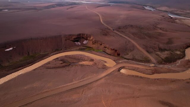 Aerial shot approaching a brown muddy river in Iceland with car driving on road. Shot in the highlands.