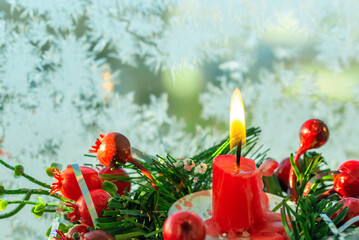 Burning red christmas candle on the background of a frozen window
