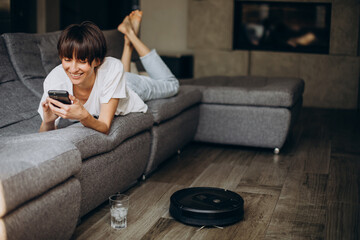 Woman using phone while vacuum robot cleaning thefloor