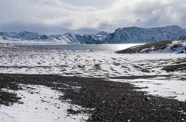 Season changing in southern Highlands of Iceland. Colorful Landmannalaugar mountains under snow cover in autumn. Frostastadavatn lake at the foot of the mountains.