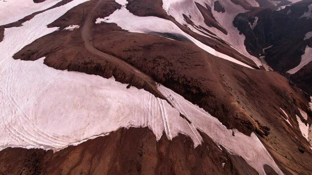 Panning up aerial shot in snowy landscape of hiking path with people. Snowy mountains in Iceland.