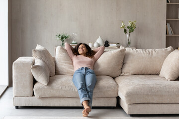 Smiling barefoot woman resting on comfortable couch at home alone, happy beautiful young female with closed eyes stretching, daydreaming or taking day nap, enjoying leisure time, no stress concept - obrazy, fototapety, plakaty