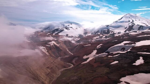 Sideways aerial shot of magnificent Iceland mountain view. Fog and clouds with snowy mountains behind. Steam rises from hot springs below.