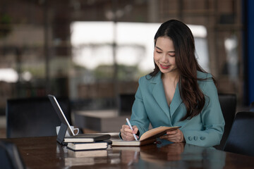 Obraz premium Businesswoman writing a note while using laptop at a table in an office.