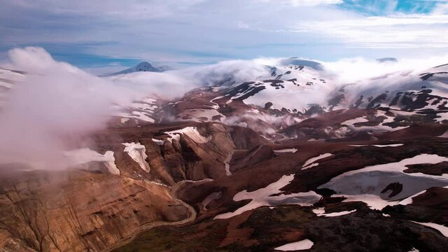Epic aerial show approaching fog and clouds in snowy mountain range. Shot in Iceland. Rivers and hot springs below.