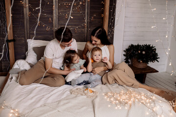 Young family playing with children on bed in bedroom decorated for christmas