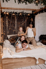 Young family playing with children on bed in bedroom decorated for christmas