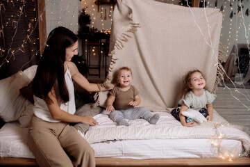 Young family playing with children on bed in bedroom decorated for christmas 