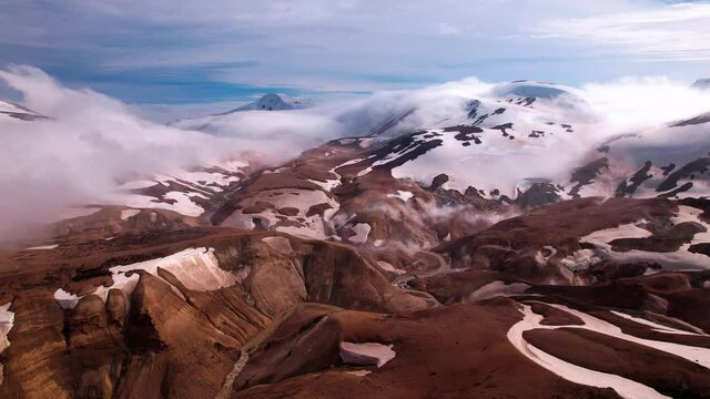 Sideways turning aerial shot over interesting snowy Icelandic landscape. Patchy snow with hills and valleys, low fog.
