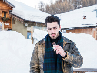 Handsome young man biting protein bar in snow