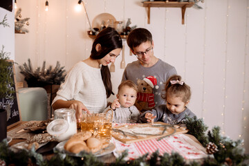 Beautiful family preparing homemade cakes on the christmas table against the backdrop of the decorations for the holiday