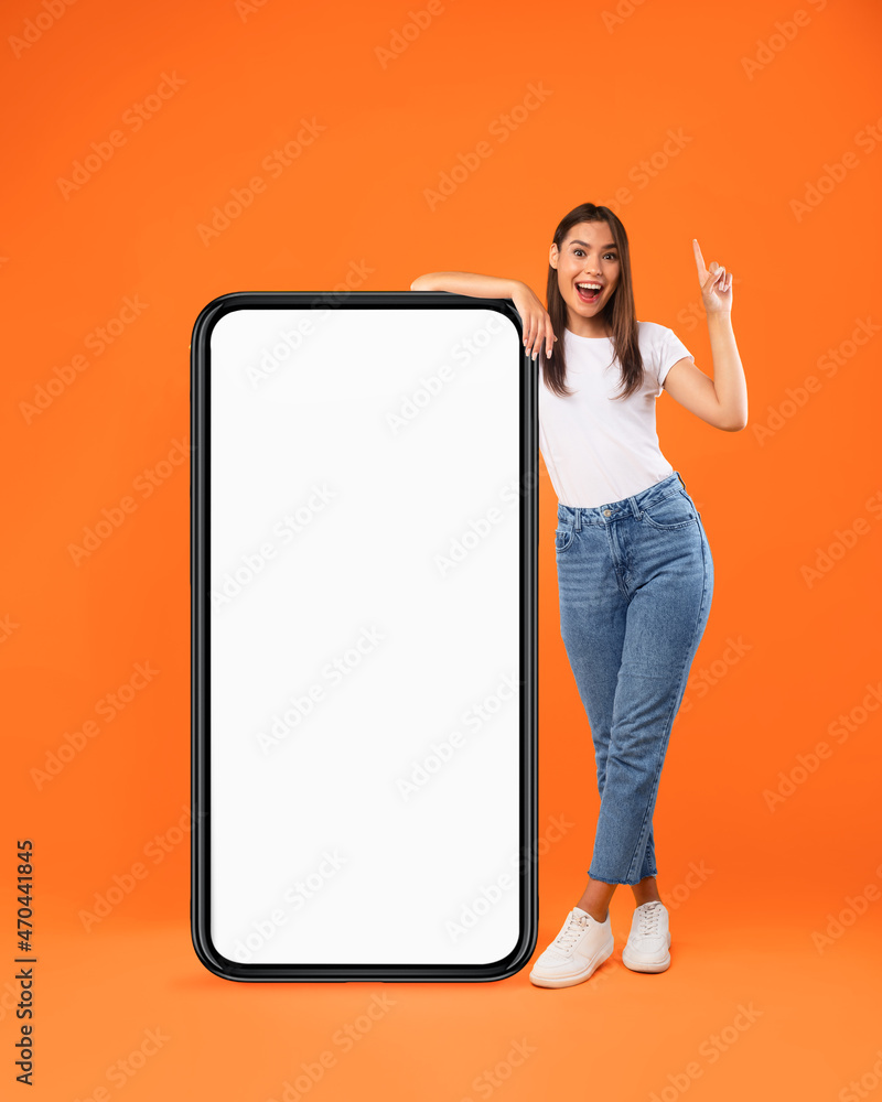 Wall mural woman pointing up leaning on big white empty smartphone screen