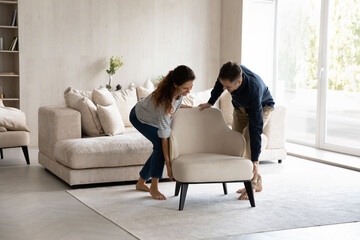 Spouses carrying modern armchair, placing furniture relocating into new home. Happy homeowners 35s...