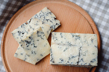 Sliced cheese with blue mold on a wooden cutting board. Cheese composition. Top view. Cheese...