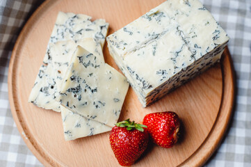 Sliced cheese with blue mold and appetizing strawberries on a wooden cutting board. Cheese composition. Top view
