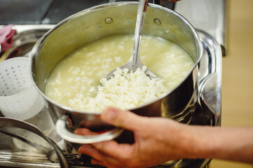 Cheesemaker cooks cheese in a steel pan, close up. Woman preparing delicious homemade cheese. process of making home-made cheese in the workshop. Film noise