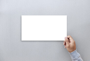 Hand holding mockup blank paper on gray background.