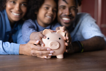 Joyful African family young couple parents and little child girl holding piggybank in hands,...