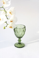 Beautiful green wine glass and orchid branch on a white background. Vertical photo. Free place.