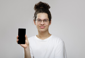 young curly male teenager holding a smartphone in his hands. Gray background