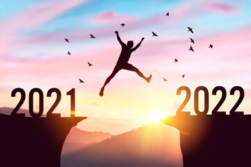 Silhouette man jumping between cliff with number 2021 to 2022 and birds flying at top of mountain. Freedom challenge and travel adventure holiday concept.