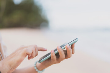 Woman hand using smart phone on tropical beach abstract background. Technology business and travel vacation concept.