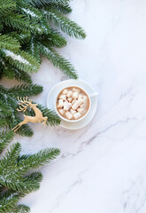 Obraz na płótnie Canvas coffee cup with marshmallows, Christmas deer toy, fir tree branches on marble background. New year and Christmas holidays concept. festive winter season. flat lay. copy space