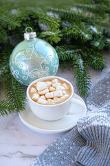 coffee cup with marshmallows, sweater, Christmas ball, fir tree branches on marble background. Christmas and new year holidays concept. festive winter season.