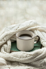 Morning coffee. A mug of hot warming drink on a book in a Warm scarf. Cozy autumn-winter concept. Blurred bokeh in the background.