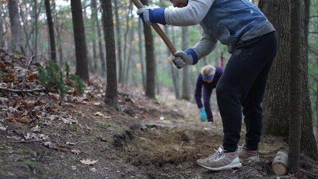 Man trail building with metal hoe to make bench cut into hill side, cut roots and clear rocks and dirt for hiking and biking path.