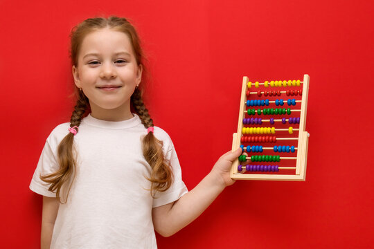 Happy little girl holds abacus in hands. On red background.