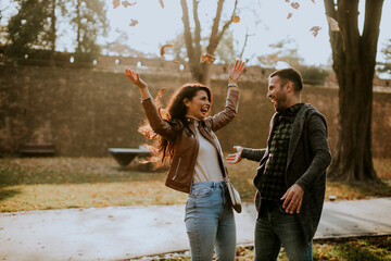 Young couple having fun with autumn leaves in the park