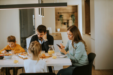 Family using mobile phones while having breakfast at dining table at apartment