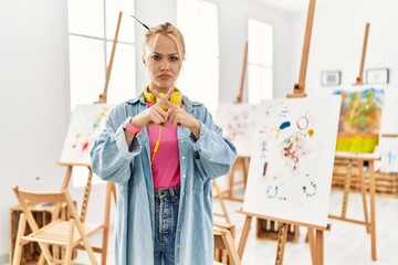 Young caucasian girl at art studio rejection expression crossing fingers doing negative sign