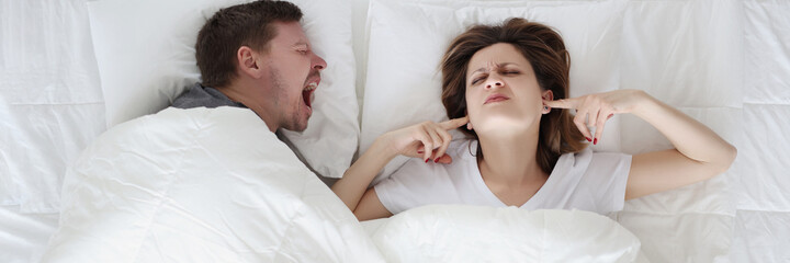 Young man lying in bed and shouting at woman with closed ears top view