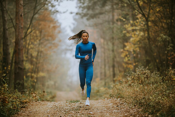 Young woman running toward camera on the forest trail at autumn