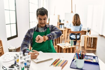 Young artist man at art studio looking at the watch time worried, afraid of getting late