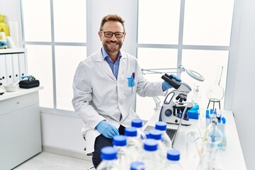 Middle age man working at scientist laboratory looking positive and happy standing and smiling with a confident smile showing teeth