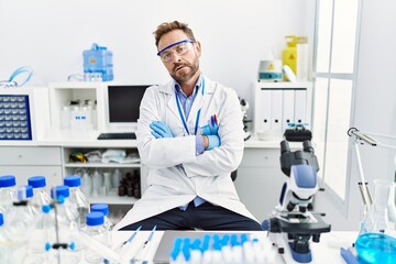 Fototapeta premium Middle age man working at scientist laboratory skeptic and nervous, disapproving expression on face with crossed arms. negative person.