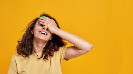 Fototapeta premium Forgetful woman with curly dark hair slapping her forehead with a happy expression as she struggling to remember something isolated over yellow background