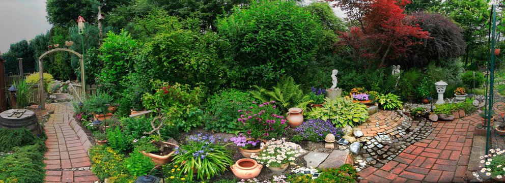 Garten im Sommer mit Blühpflanzen, Büschen und Deko
