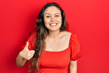 Young hispanic girl wearing casual clothes smiling happy and positive, thumb up doing excellent and approval sign