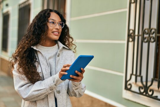 Young latin woman smiling happy using touchpad at the city.