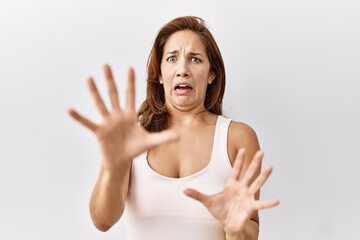 Middle age hispanic woman standing over isolated background afraid and terrified with fear expression stop gesture with hands, shouting in shock. panic concept.