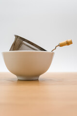 metal tea strainer in a white stoneware bowl on a wooden tabletop background