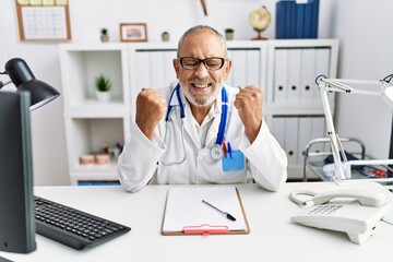 Mature doctor man at the clinic excited for success with arms raised and eyes closed celebrating victory smiling. winner concept.