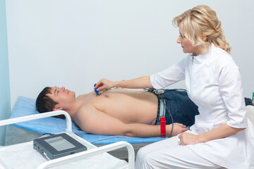 Obraz premium A cardiologist doctor applies sensors to the naked body of a man lying on a couch during an electrocardiography procedure in a hospital