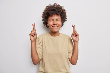 Anticipating important results. Hopeful curly haired woman bites lips keeps fingers crossed...