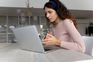 Close up serious businesswoman in headphones using laptop, chatting online with colleagues or business partners by video call, looking at computer screen, student or teacher engaged in webinar