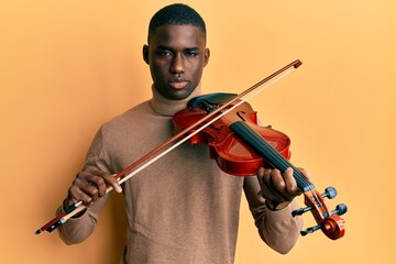 Young african american man playing violin relaxed with serious expression on face. simple and...